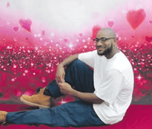 John McGraw seated in a white T-shirt in front of a heart backdrop