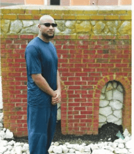 John McGraw standing in a blue outfit beside a brick wall