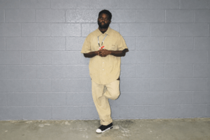 Ja’quez Butler standing in front of a gray wall, full-length portrait