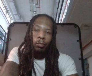 Joshua Carse seated in a white shirt with long locs